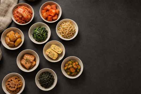 An assortment of colorful banchan in cream ceramic dishes on a charcoal table.